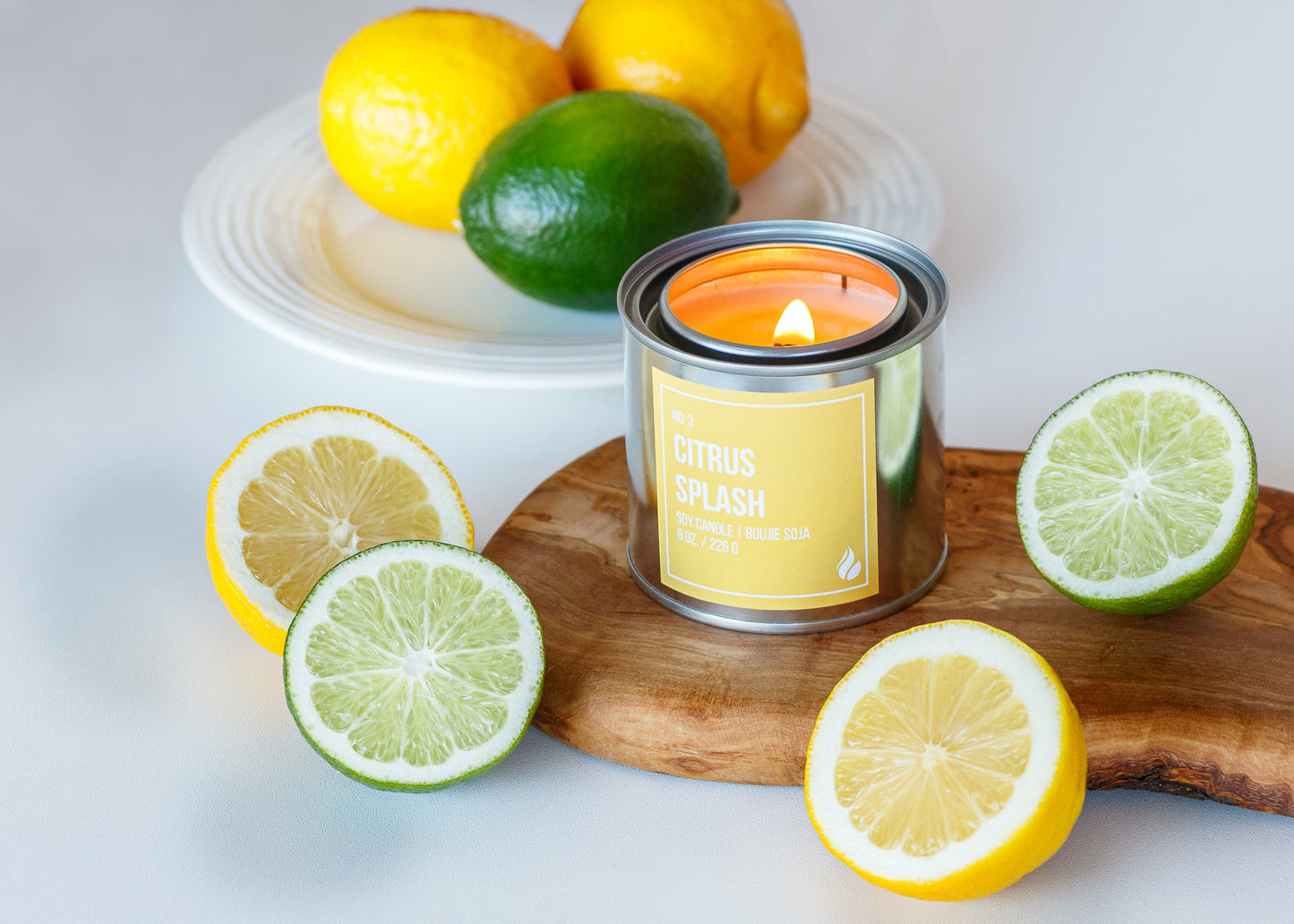Picture of Citrus Splash Paint Can Candle on a wooden board next to citrus fruits against a white background.