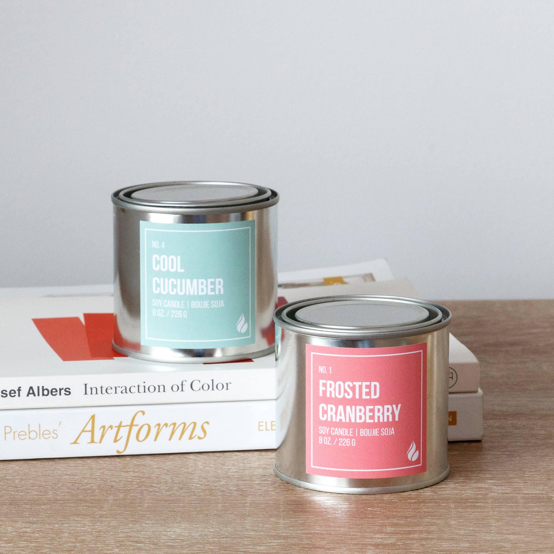 A Cool Cucumber and Frosted Cranberry paint can candle on a wooden surface with books in the background