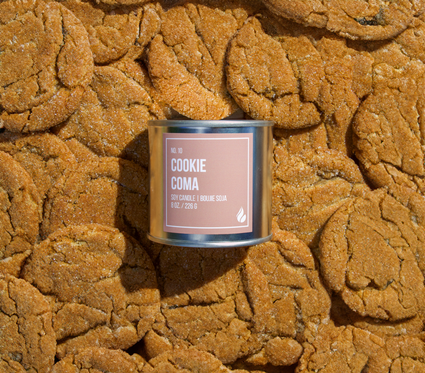 Picture of cookies covering the entire background with a Cookie Coma candle place on top, label facing screen.