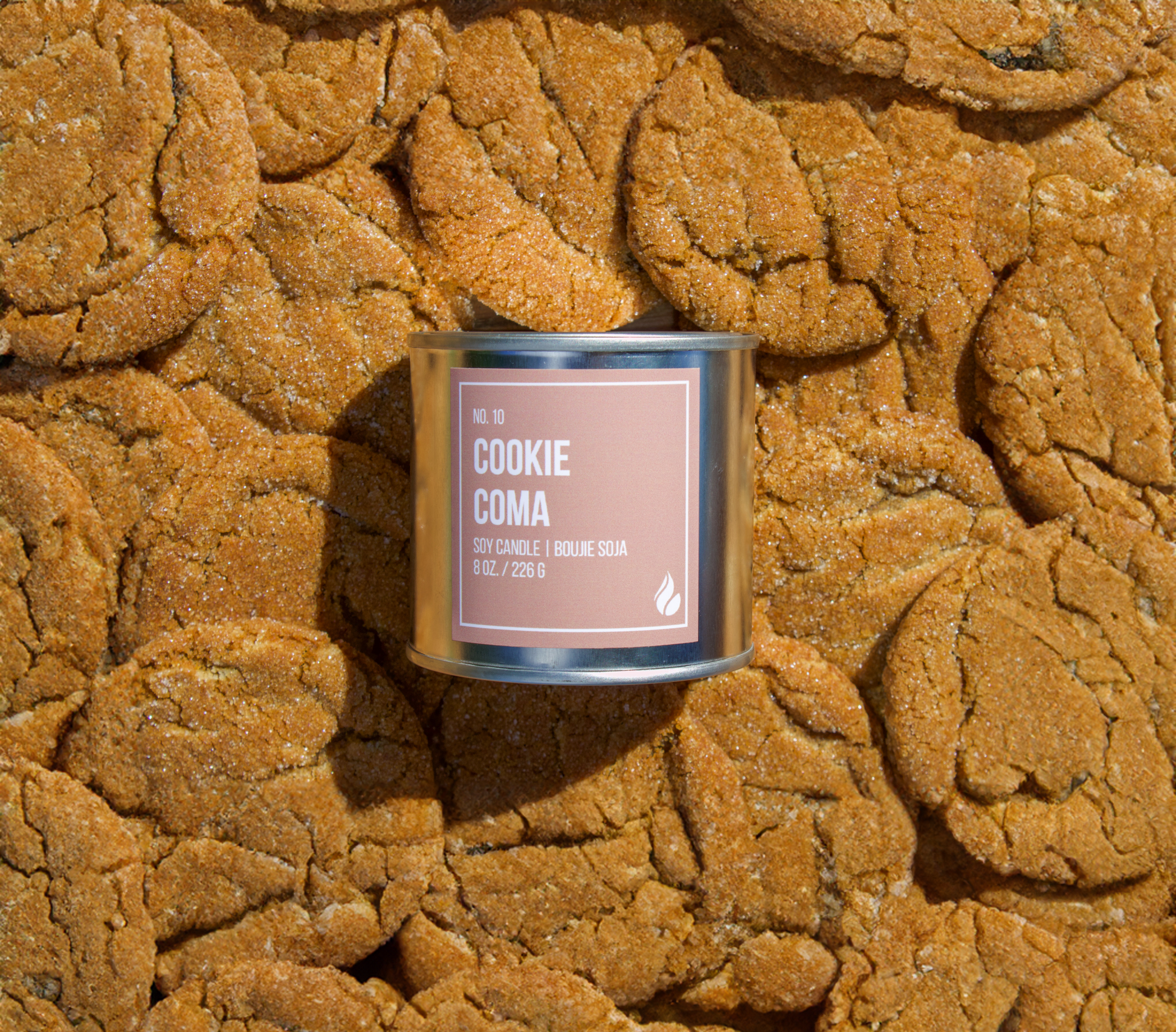 Picture of cookies covering the entire background with a Cookie Coma candle place on top, label facing screen.
