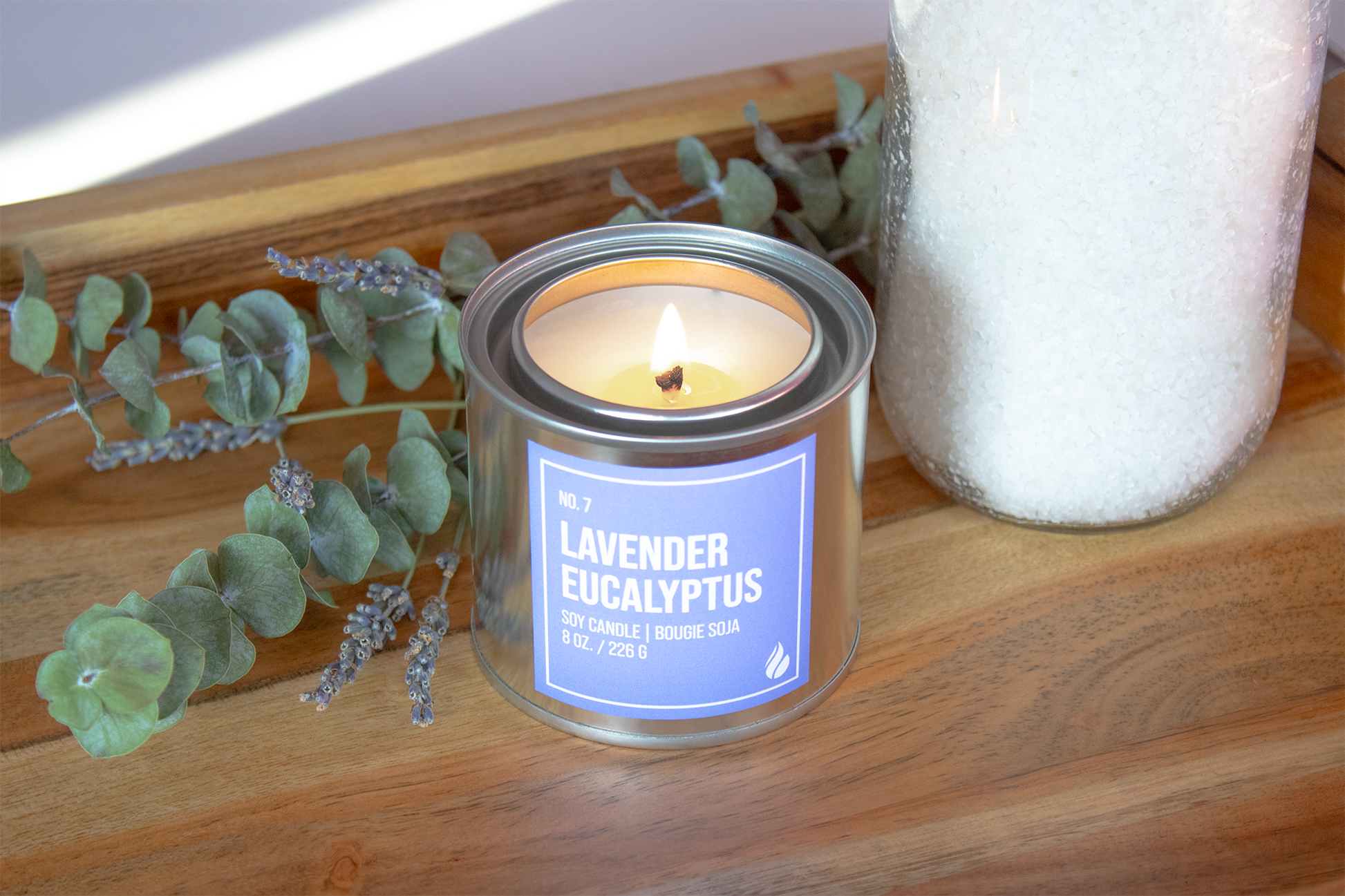 Product photograph of a Lavender Eucalyptus Paint Can Candle on a wooden tray with eucalyptus and a jar as props.
