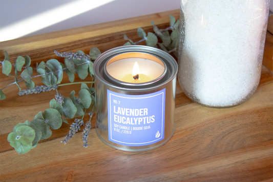 Product photograph of a Lavender Eucalyptus Paint Can Candle on a wooden tray with eucalyptus and a jar as props.