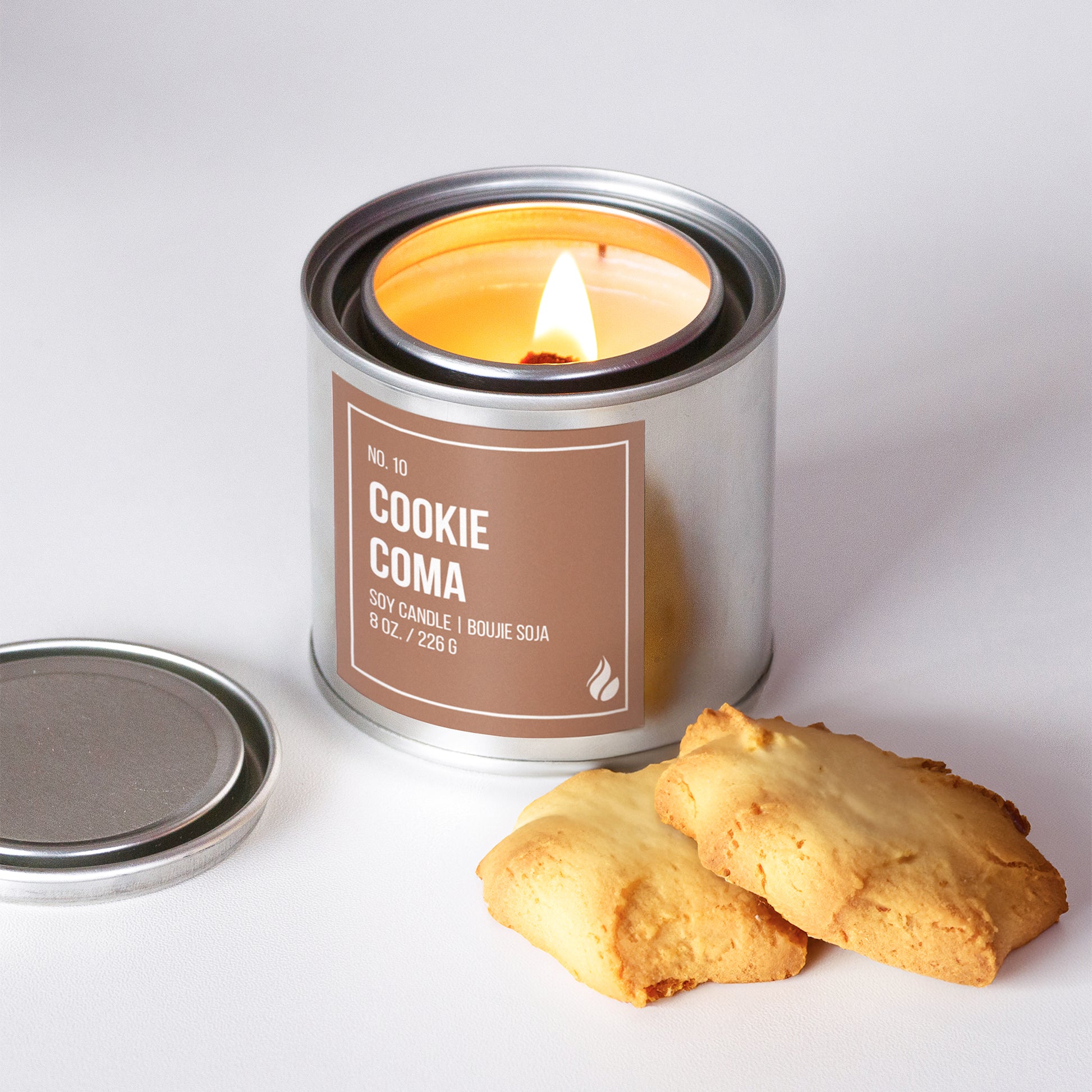 Picture of a burning Cookie Coma candle with a candle lid located on the left and a group of cookies featured on the bottom right.