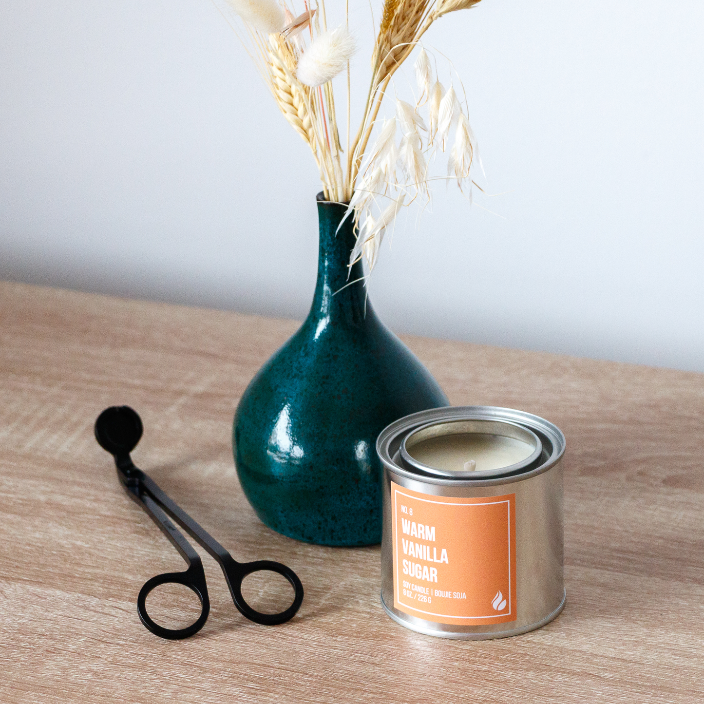 Warm Vanilla Sugar paint can candle next to a decorative vase with dried plants, and black wick trimmer on a wooden surface.