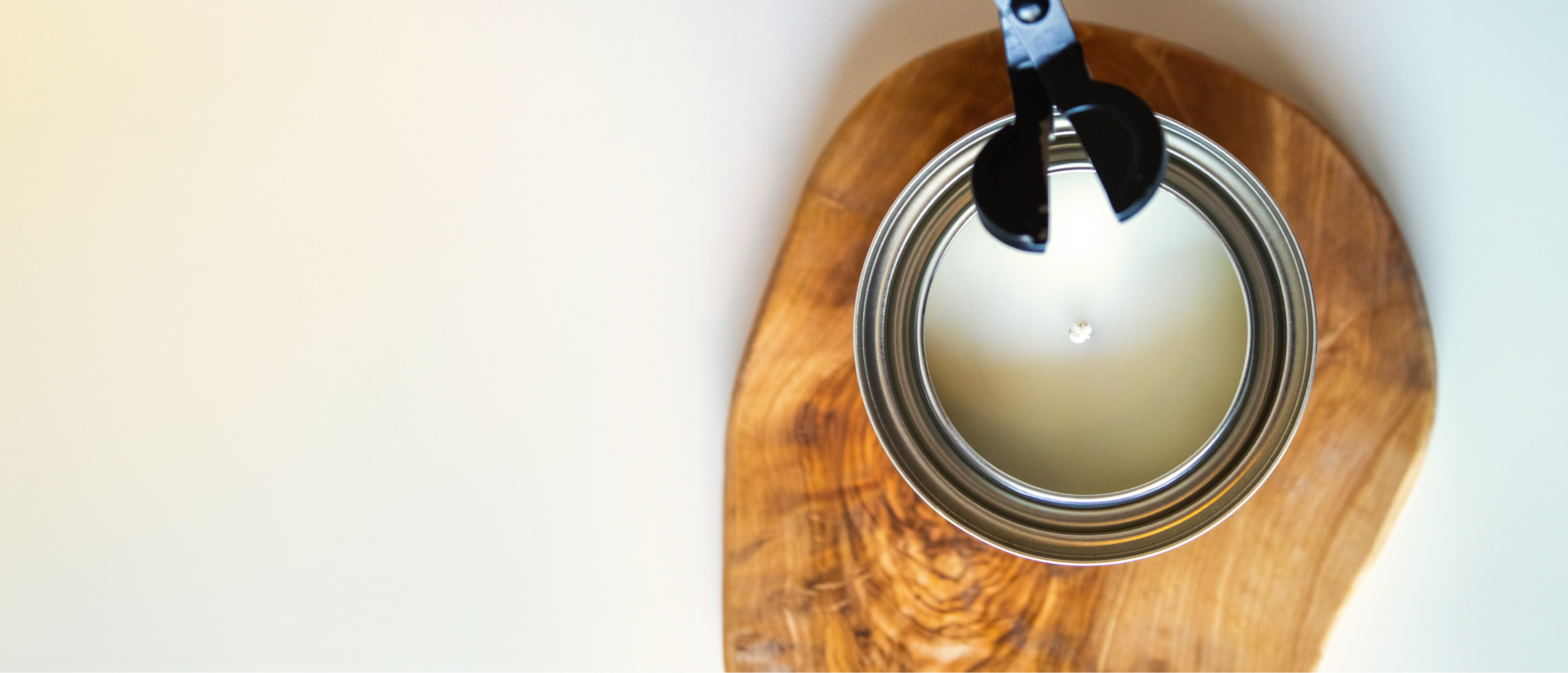Picture of a candle on top of a wooden coaster with a black wick trimmer featured on top.