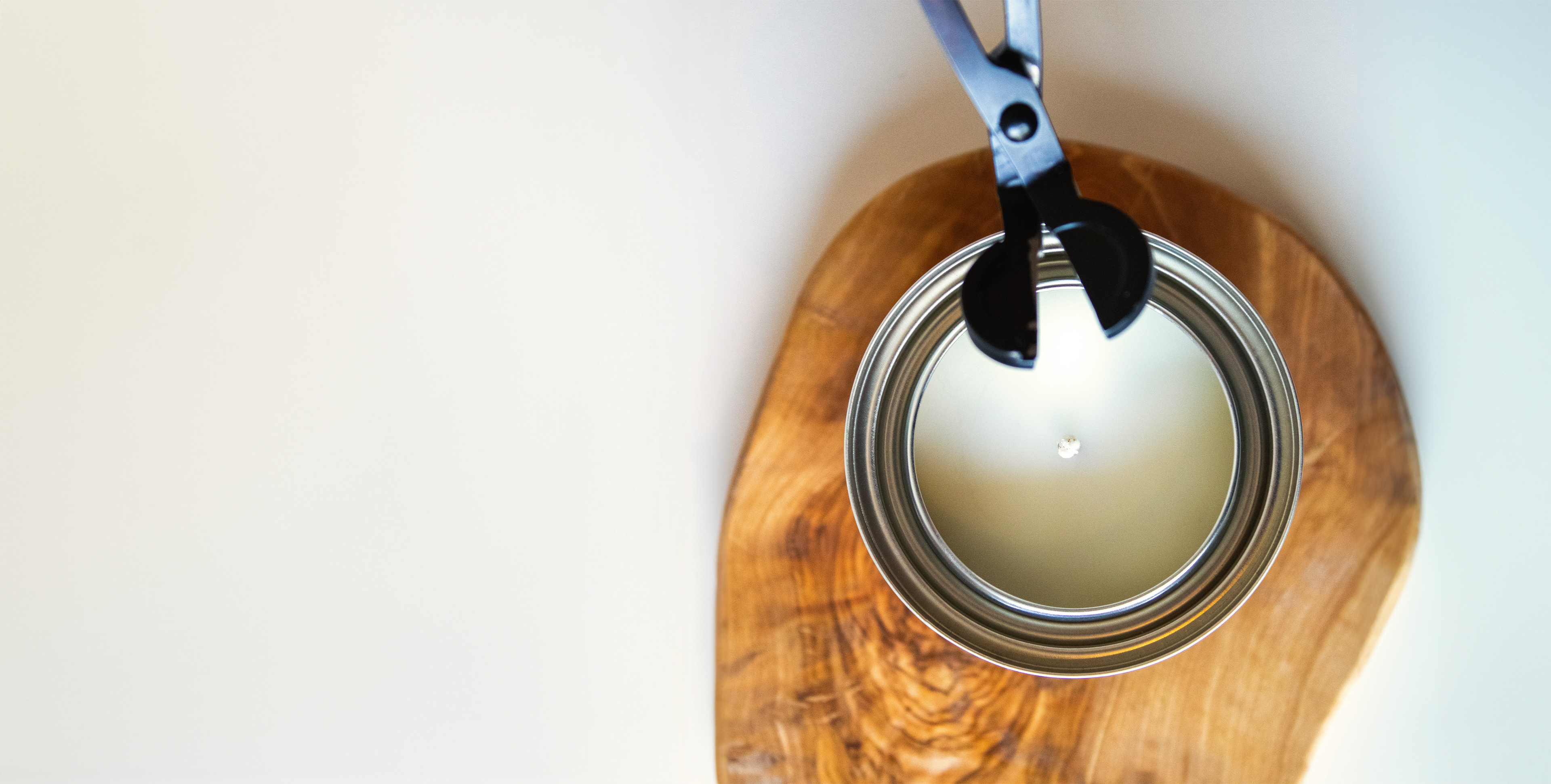 Picture of candle on wooden plate featuring a black wick trimmer against a white background.